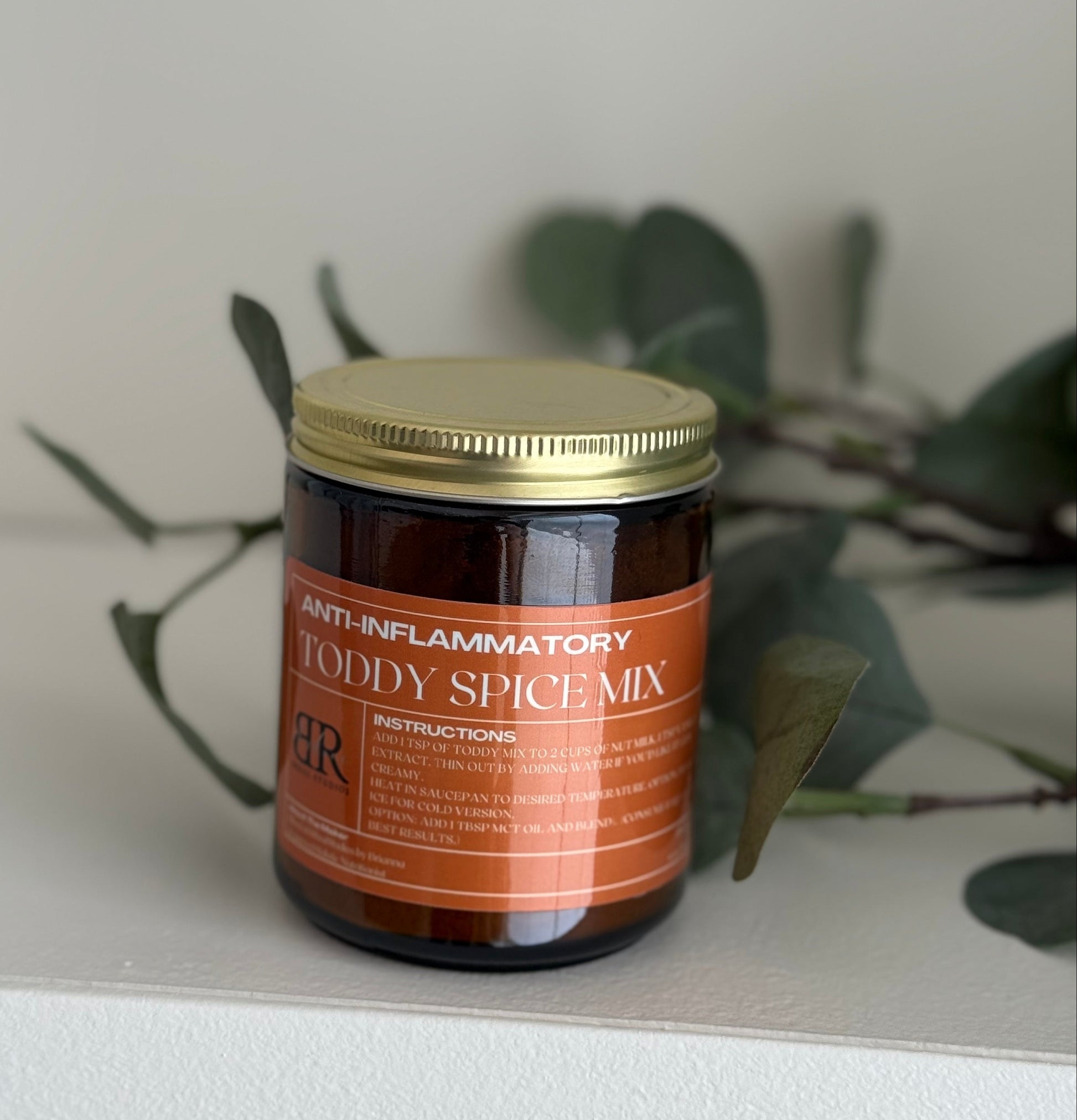 Jar of anti-inflammatory toddy spice mix on a neutral background with greenery