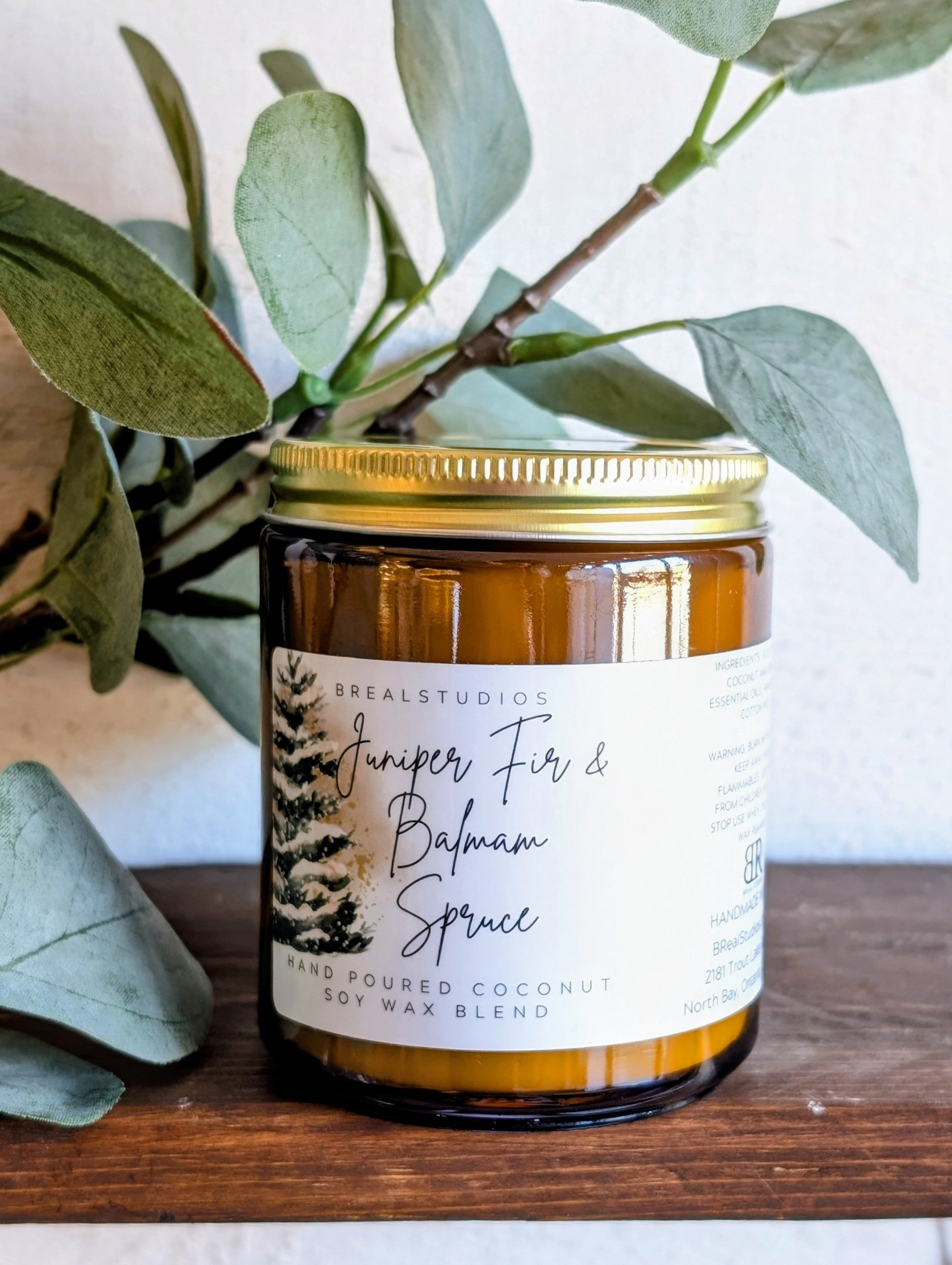 Candle jar with a label on a wooden surface with green leaves in the background